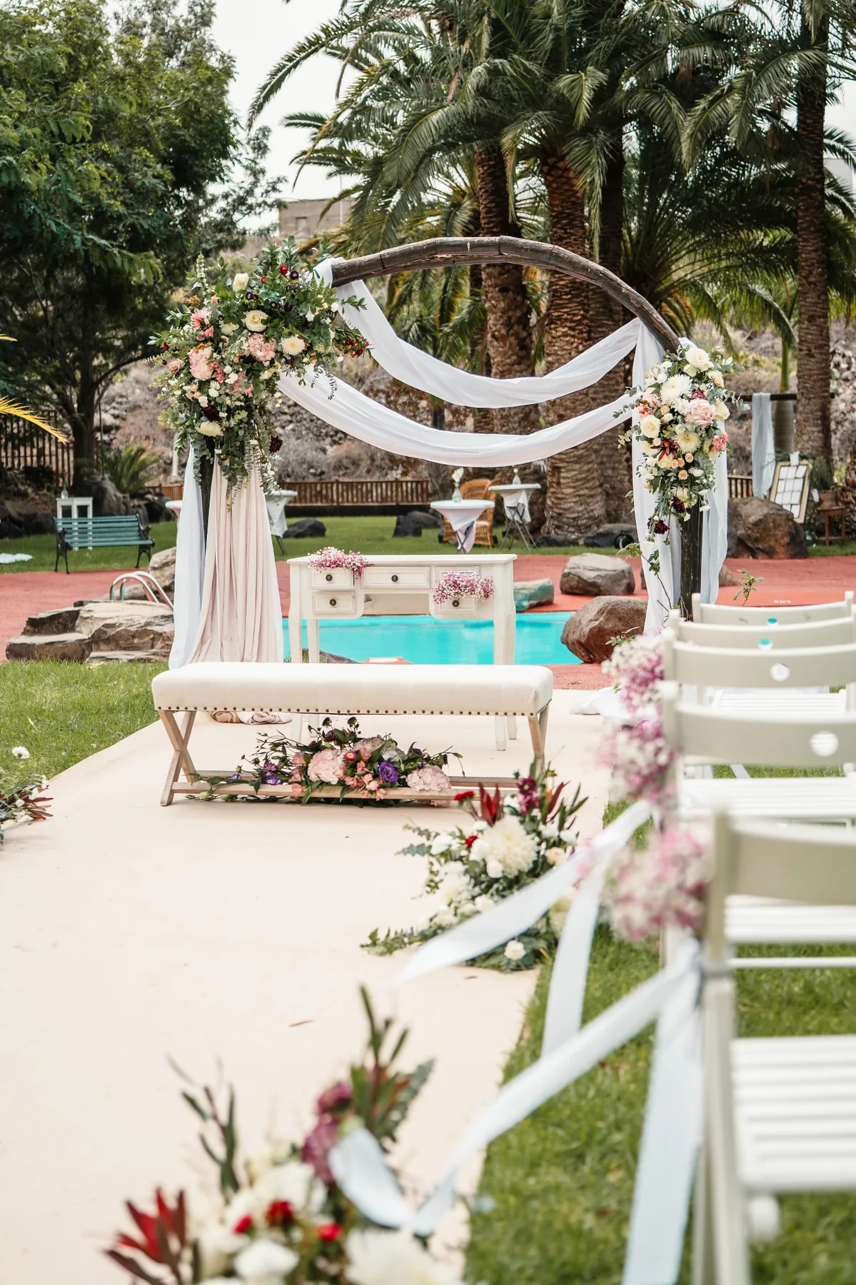 Arco floral con telas blancas junto a la piscina en ceremonia de boda en Hacienda de Anzo, Gran Canaria