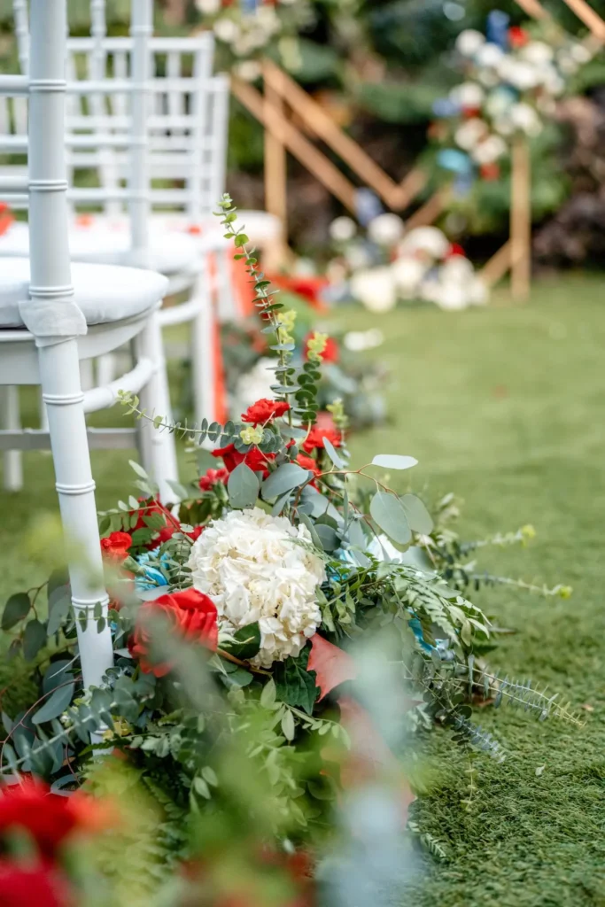 Hortensia blanca y rosas rojas con eucalipto en el suelo del pasillo nupcial, sillas blancas al fondo