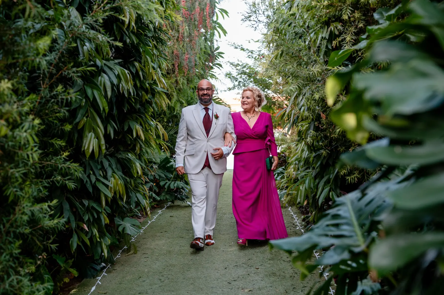 Novio caminando con su madre por pasillo rodeado de vegetación